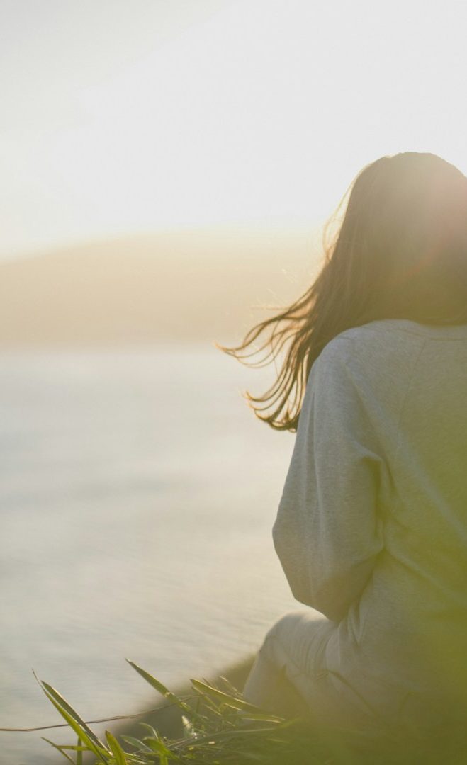 Frau sitzt in der Düne und blickt auf das Meer